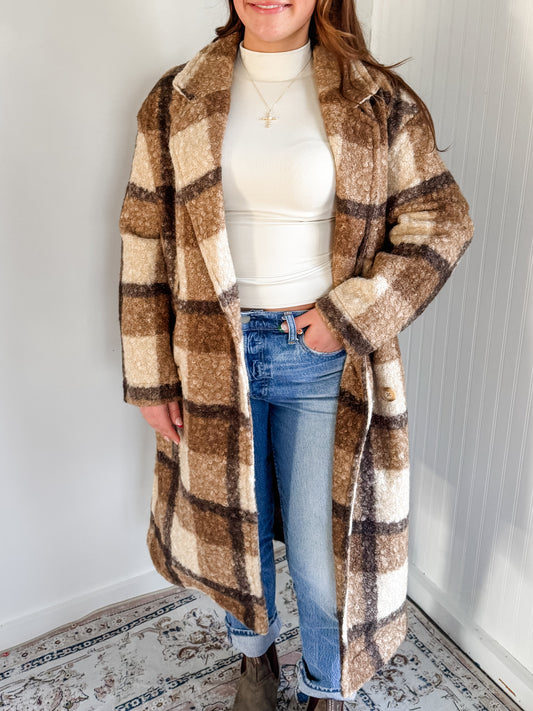 Woman wearing a plaid coat in a room with a white wall and patterned rug.