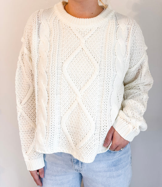 Person wearing a cream knitted sweater and light blue jeans against a plain background