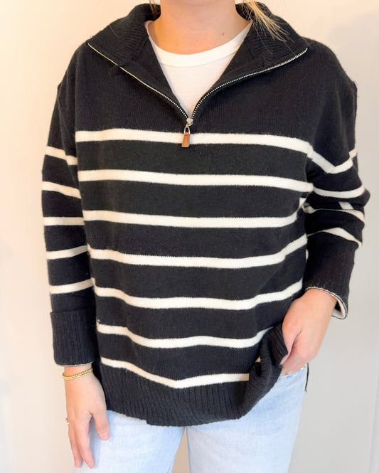 Person wearing a black and white striped sweater with a zipper on a plain background