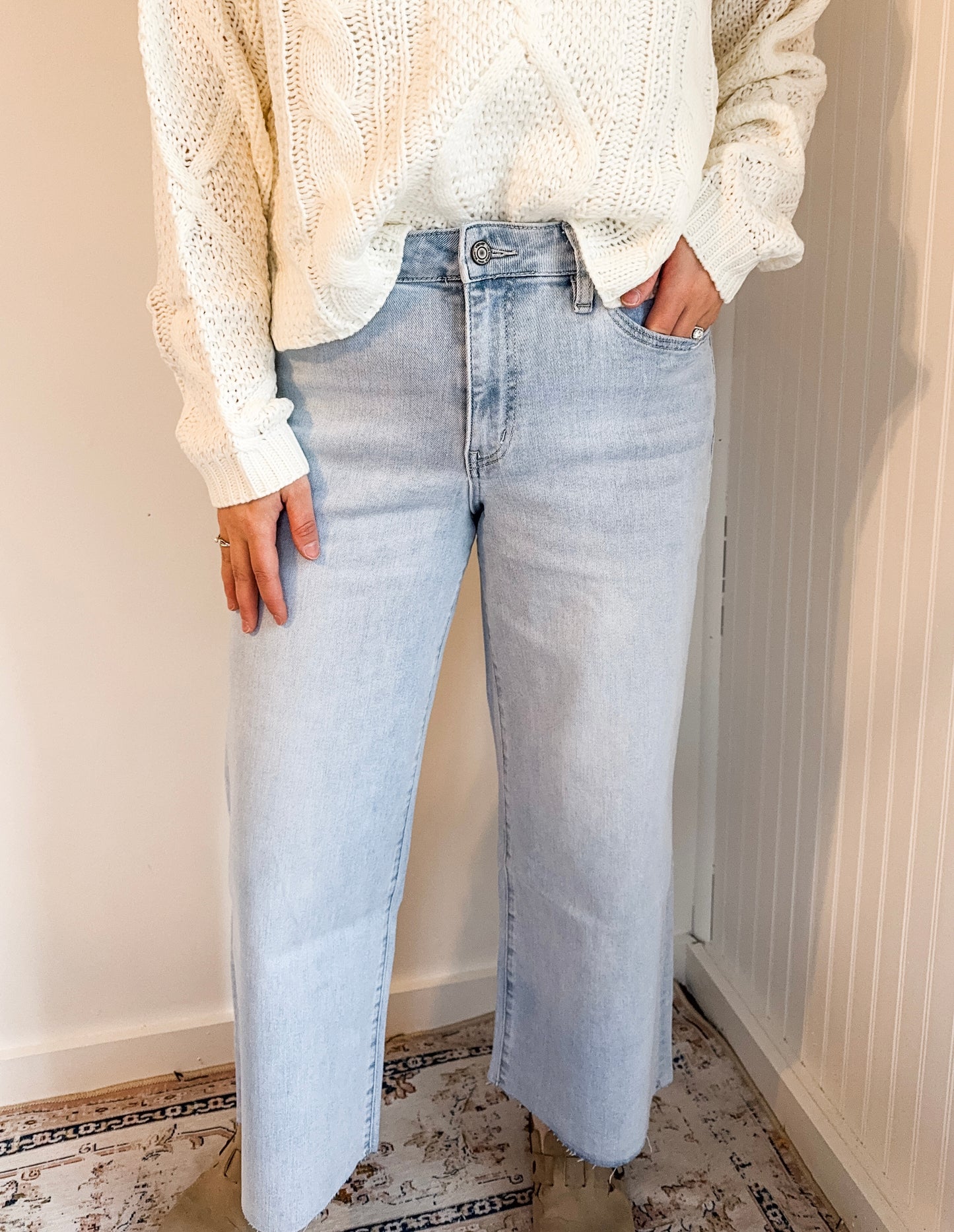 Person wearing light blue jeans and a white textured sweater indoors.