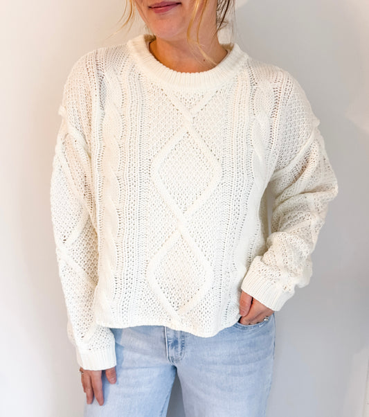 Person wearing a white knit sweater and light blue jeans against a plain background