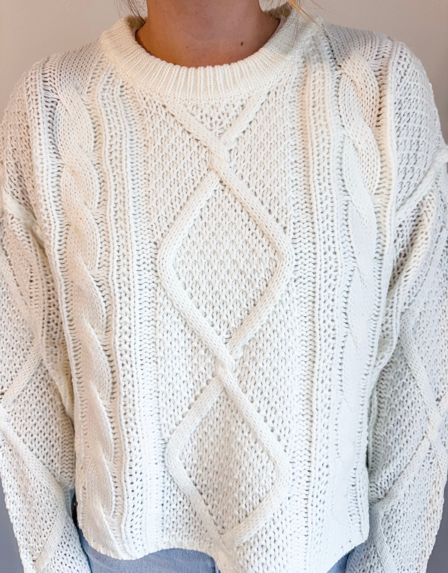 Close-up of a person wearing a white cable knit sweater against a neutral background