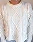 Close-up of a person wearing a white cable knit sweater against a neutral background