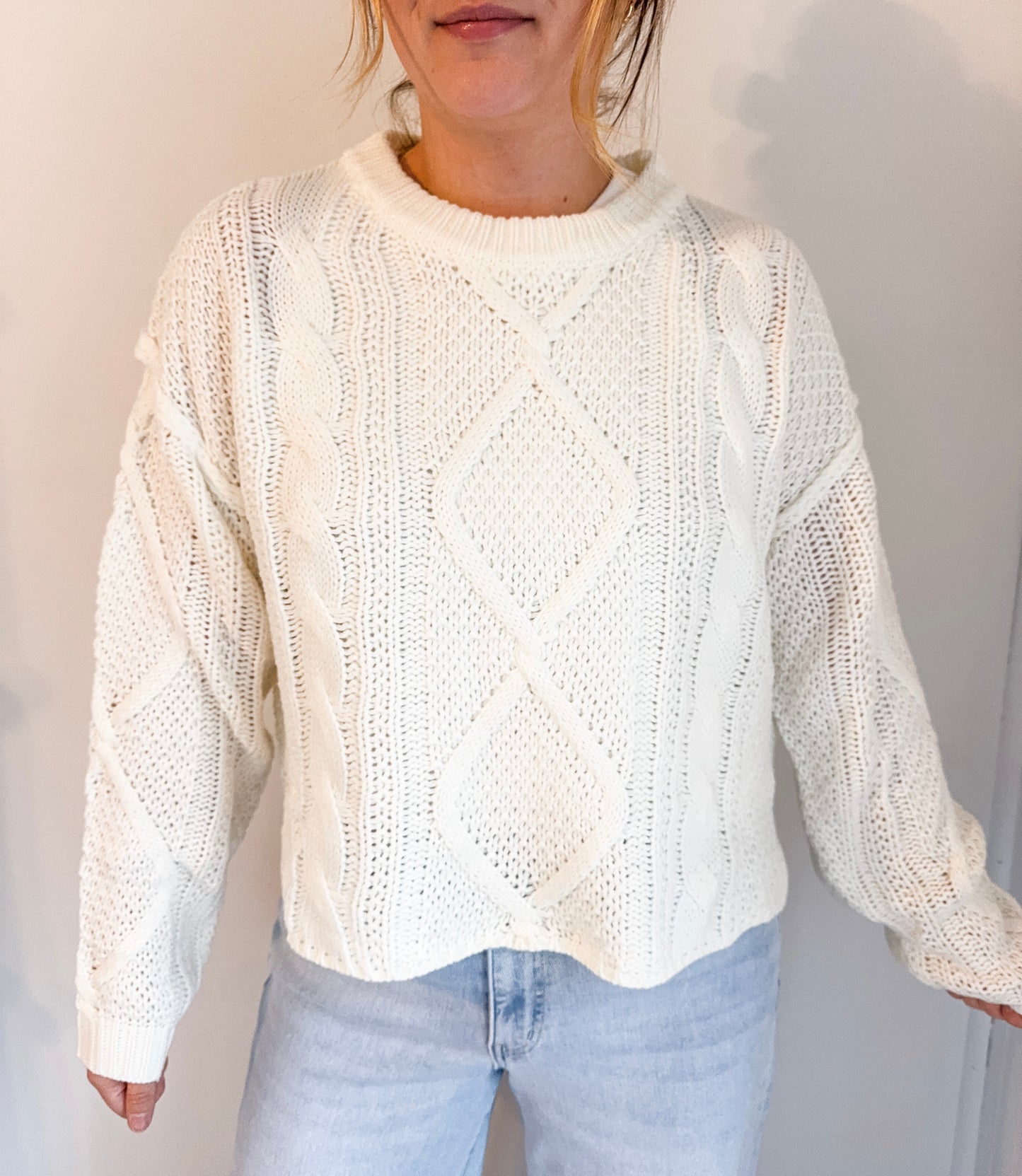Person wearing a white knitted sweater and light blue jeans against a plain background