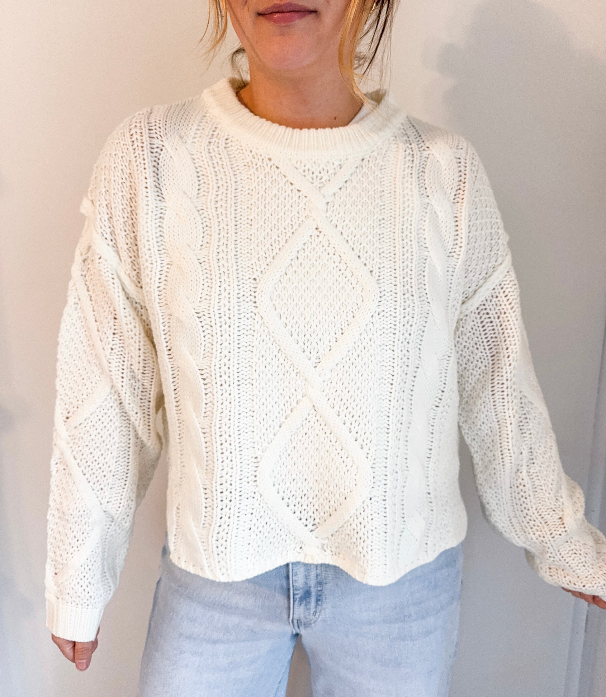 Person wearing a white knitted sweater and light blue jeans against a plain background