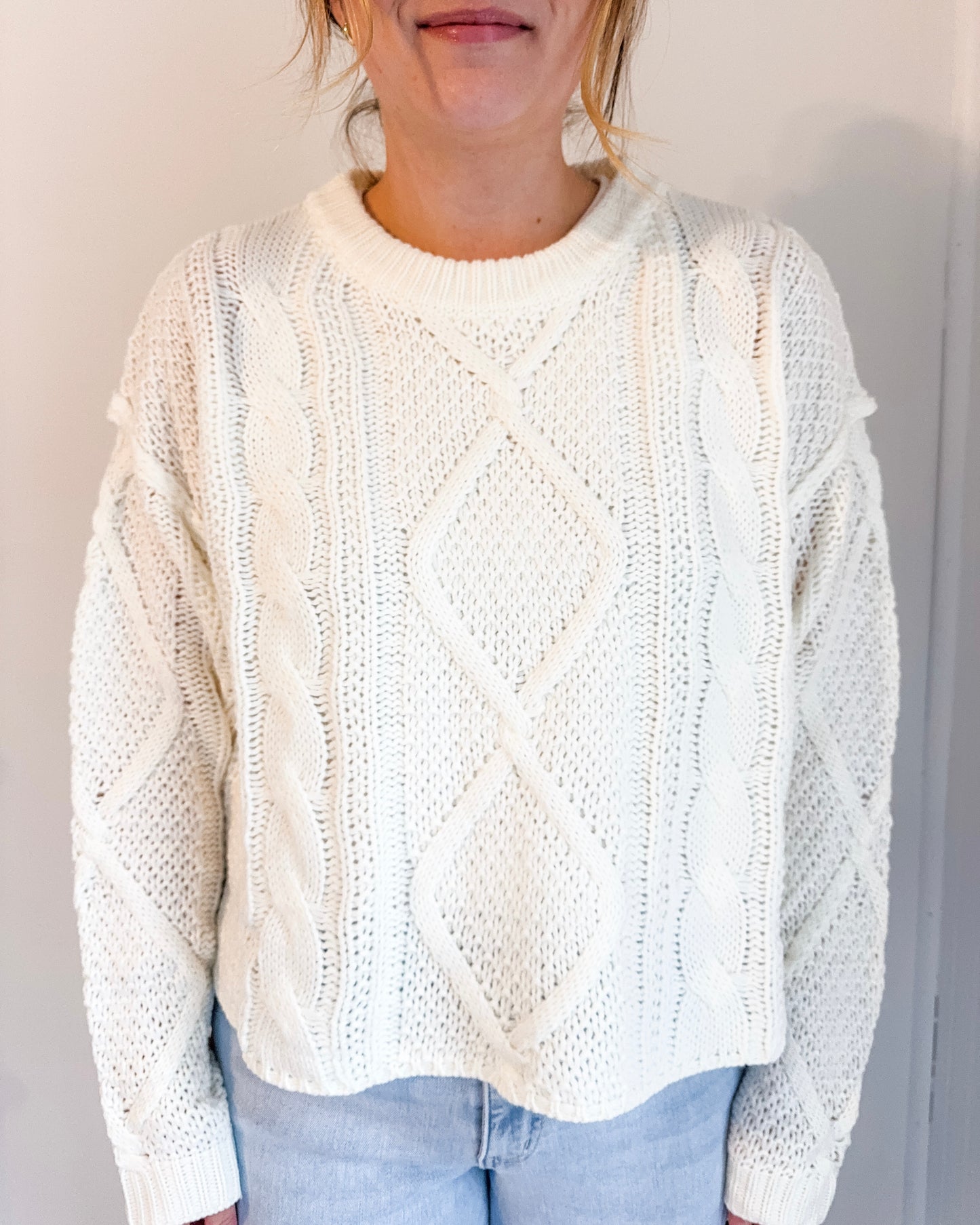 Person wearing a white cable knit sweater against a plain background